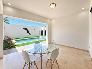 A modern interior with a glass table and chairs, a pool outside, and a white wall with a black map. - Delfines Duplex Home shared pool (La Paz)