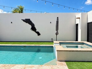 A swimming pool with clear blue water, a white wall with a black map, and string lights above. - Delfines Duplex Home shared pool (La Paz)