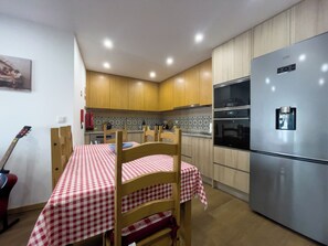A kitchen with wooden cabinets, a stainless steel refrigerator, a checkered tablecloth, and a guitar leaning against the wall. - House Sleeps 4 with Parking and Balcony (viseo)