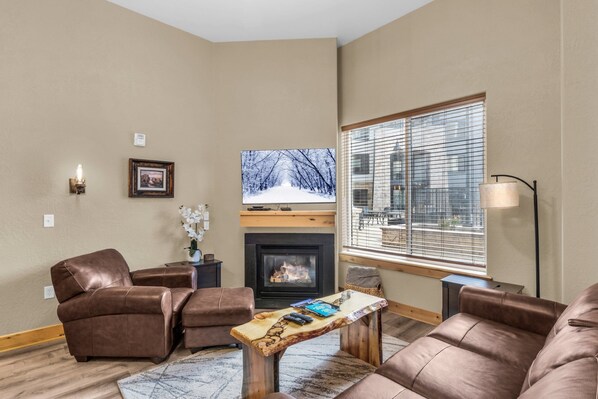 A living room with leather sofas, a fireplace, a television, and a large window with blinds. - Silverado 106 | Walk to Lifts | Pool | Hot Tub | Fireplace | Sleeps 4 (Park City)