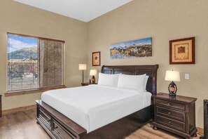 A bedroom with a large bed, two bedside tables with lamps, a window with blinds, and two framed pictures on the wall. - Silverado 106 | Walk to Lifts | Pool | Hot Tub | Fireplace | Sleeps 4 (Park City)