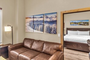 A hotel room with a brown leather sofa, a bed with white bedding, and two paintings on the wall. - Silverado 106 | Walk to Lifts | Pool | Hot Tub | Fireplace | Sleeps 4 (Park City)