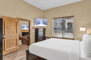 Ein Hotelzimmer mit Bett, Fernseher, Kommode und einem Fenster mit Jalousien.