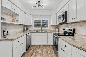 A kitchen with white cabinets, a stainless steel range, and a window with blinds. - 🌴Palm Breeze Retreat- Home with a pool, hot tub & game room near Clearwater Beach! (Largo)