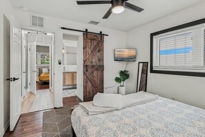 A bedroom with a bed, a TV mounted on the wall, a sliding barn door, and a window with blinds. -   🌴Palm Breeze Retreat- Home with a pool, hot tub & game room near Clearwater Beach! (Largo)