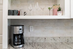 A kitchen with a coffee maker, mugs, wine glasses, and a potted plant on the shelf. - 🌴Palm Breeze Retreat- Home with a pool, hot tub & game room near Clearwater Beach! (Largo)