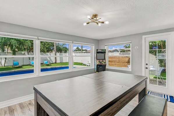 A spacious room with a pool view, a ceiling fan, and a gaming console. - 🌴Palm Breeze Retreat- Home with a pool, hot tub & game room near Clearwater Beach! (Largo)