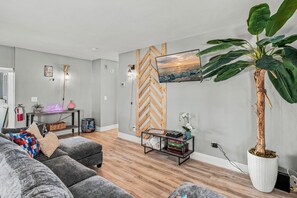Ein modernes Wohnzimmer mit einem grauen Sofa, einer Wand mit Holz-Fischgrätmuster, einer großen Topfpflanze und einem flachbildfernseher, der an der Wand befestigt ist.