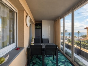 Un balcon avec une table et des chaises, une horloge, une porte et une vue sur la plage et l’océan.