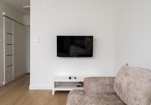A modern living room with a flat-screen TV mounted on a white wall, a white entertainment unit below, and a patterned sofa. - Plac Grzybowski Skyline Studio (Warszawa)