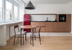 A modern kitchen with a dining area, featuring a red refrigerator, a black pendant light, and wooden cabinets. - Plac Grzybowski Skyline Studio (Warszawa)