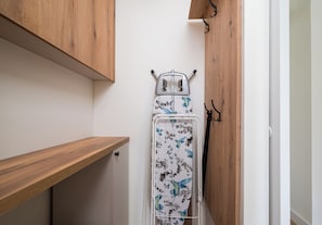 A compact room with a wooden shelf, a white wall, and a metal drying rack with a floral pattern. - Plac Grzybowski Skyline Studio (Warszawa)