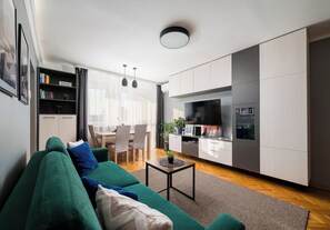 A modern living room with a green sofa, a dining table with chairs, and a kitchen area with cabinets and a TV. - Dolny Mokotów Signature Apartment (Warszawa)