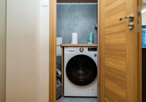 A compact laundry room with a front-loading washing machine and a wooden door. - Dolny Mokotów Signature Apartment (Warszawa)