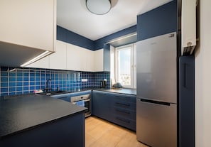 A modern kitchen with a stainless steel refrigerator, a built-in oven, and a window providing natural light. - Dolny Mokotów Signature Apartment (Warszawa)