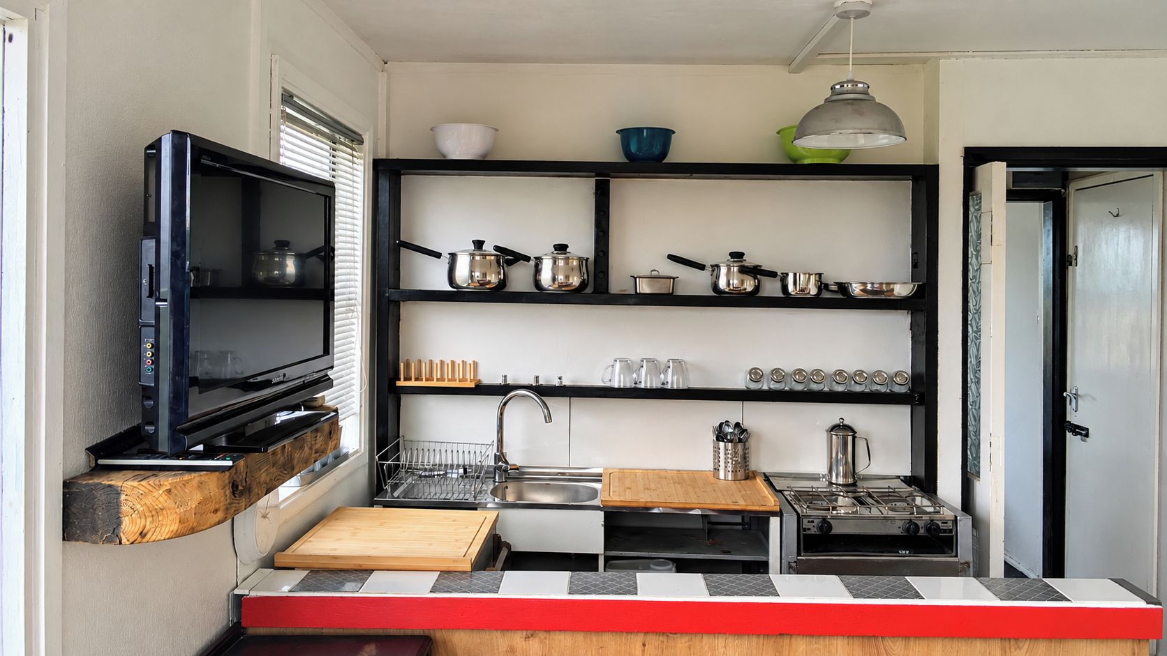Une cuisine compacte équipée d’une cuisinière intégrée, d’un évier et d’un téléviseur posé sur une étagère.
