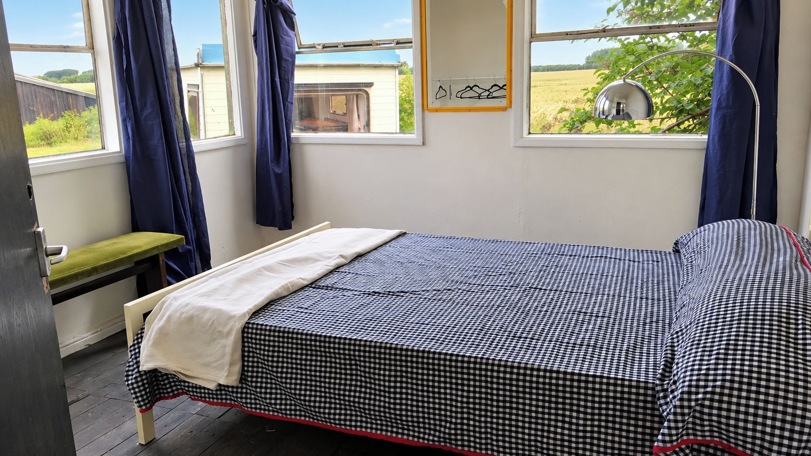 A bedroom with a checkered bedspread, a bench, and a view of a field through the window.