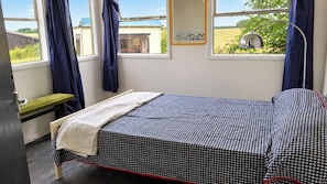 A bedroom with a checkered bedspread, a bench, and a view of a field through the window. - Farm Stay, Sleeps 4 w/ Parking near Peterborough (Spalding)