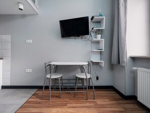 A modern kitchen with a built-in TV, white cabinetry, and a small dining area with a table and two chairs. - Legionów Central Studio #4 (Łódź)