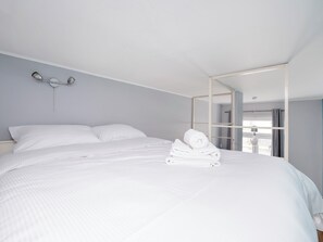 A neatly made bed with white linens and a rolled towel on top, a bedside table, and a wall-mounted light fixture. - Legionów Central Studio #4 (Łódź)