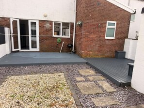 A patio area with a wooden deck, a gravel garden bed, and a brick wall. - Blissful Retreat, families travellers or contractors (Bridgend)