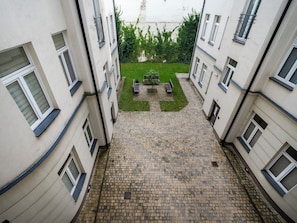 Ein Innenhof mit gepflastertem Weg, Bänken und einer Rasenfläche, umgeben von Gebäuden mit zahlreichen Fenstern.