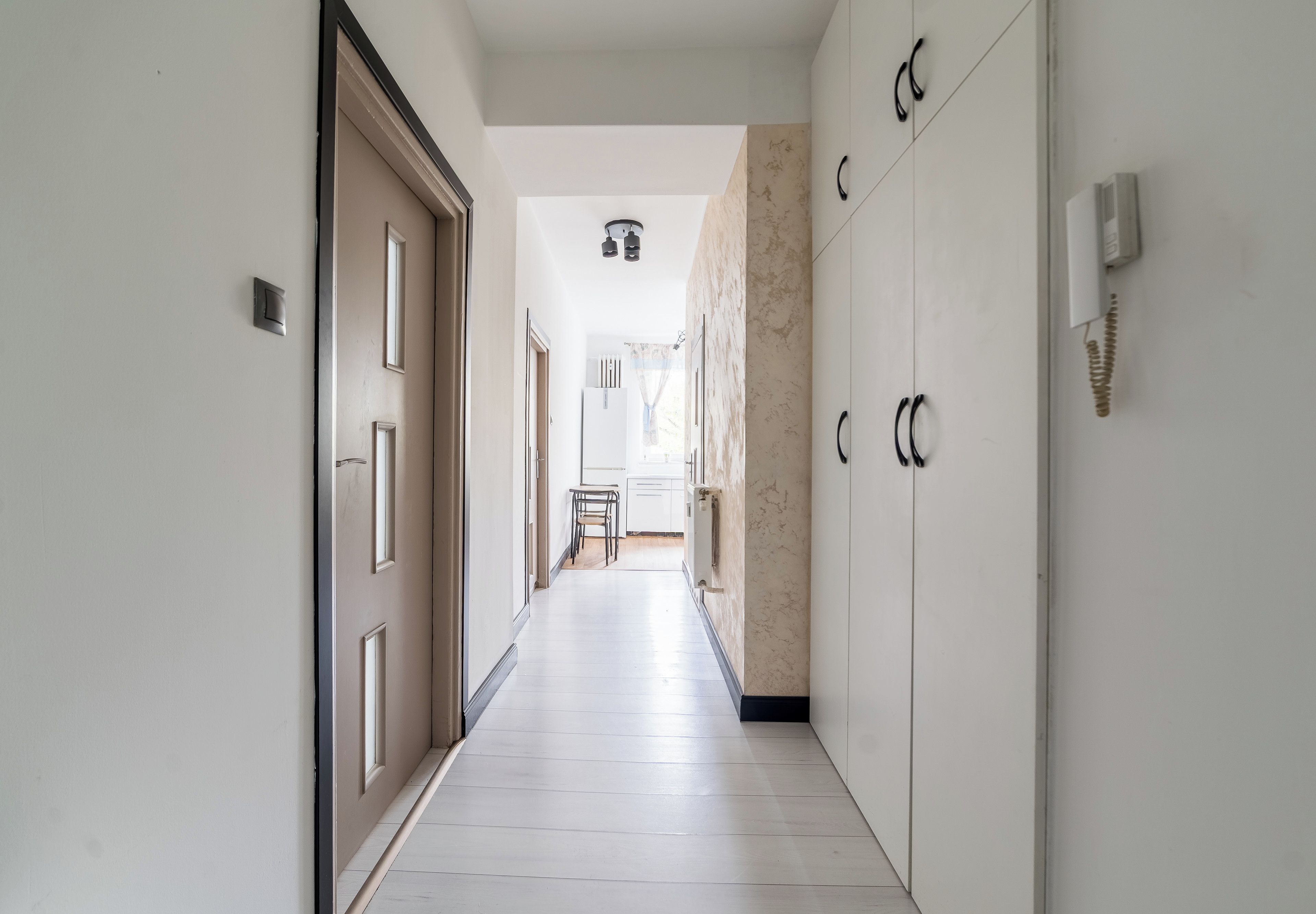 A corridor with a door on the left, a chair in the middle, and cabinets on the right.