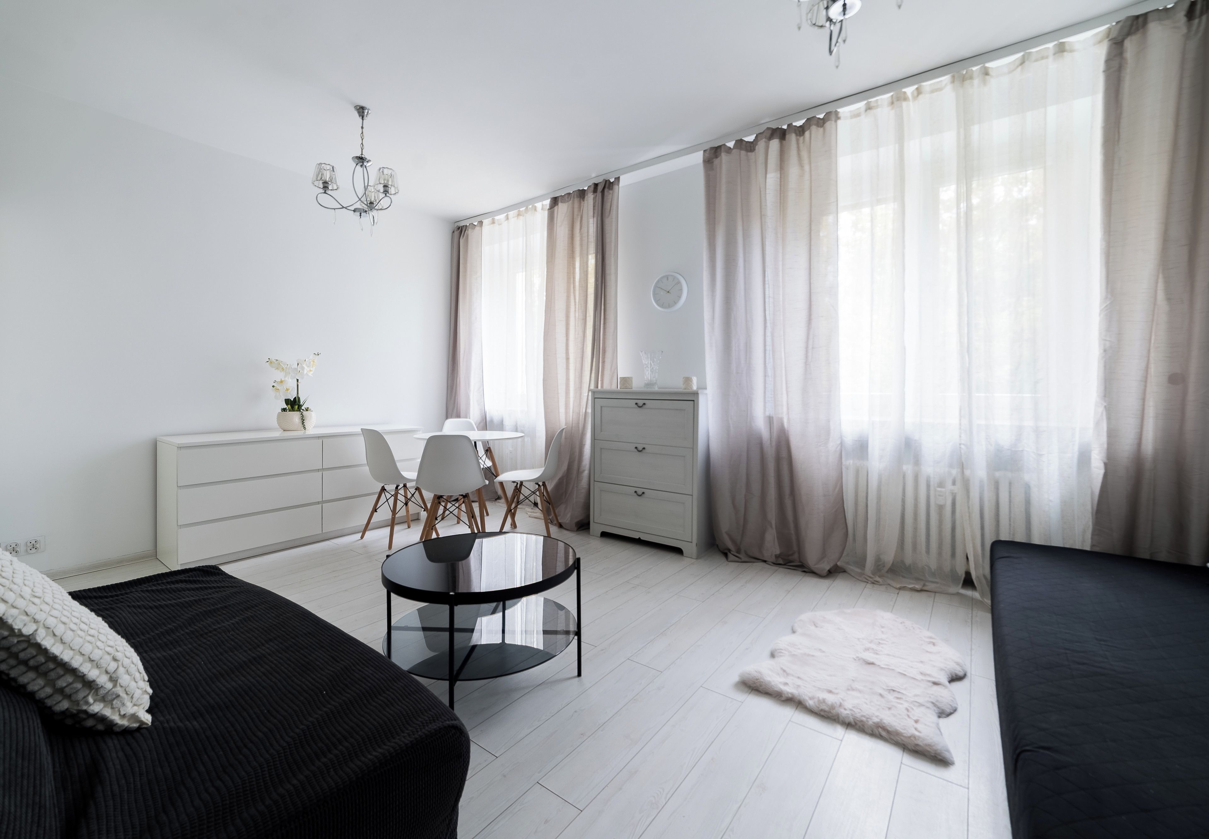 Ein modernes Schlafzimmer mit Bett, Schreibtisch, Stuhl, Kommode und einem großen Fenster mit Vorhängen.