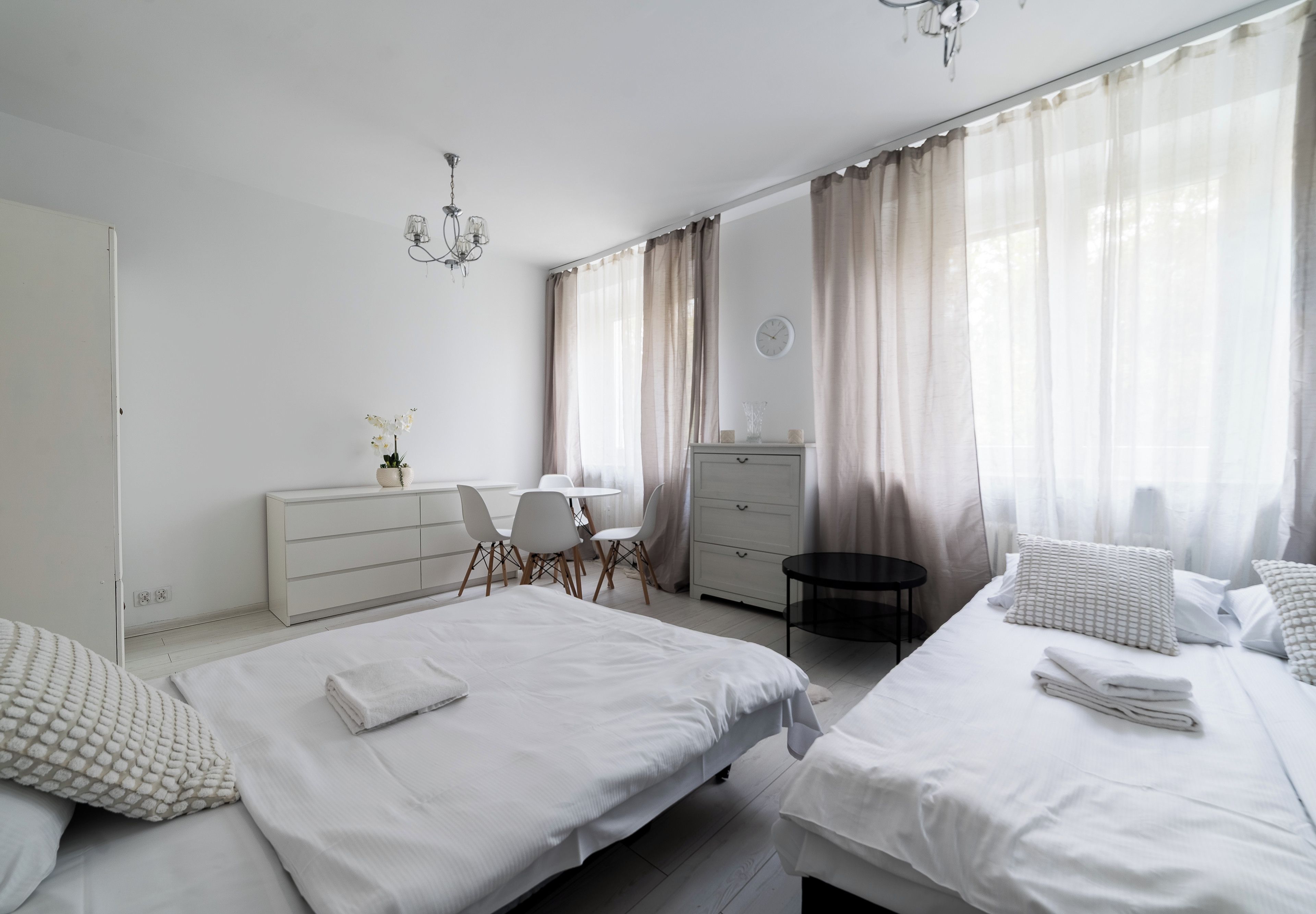 Ein modernes Schlafzimmer mit zwei Betten, einem Schreibtisch, einem Stuhl, einer Kommode und einer Wanduhr.