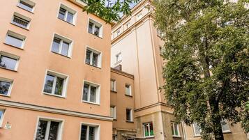 Ein mehrstöckiges Gebäude mit einer beigefarbenen Fassade und mehreren Fenstern, im Vordergrund steht ein Baum.