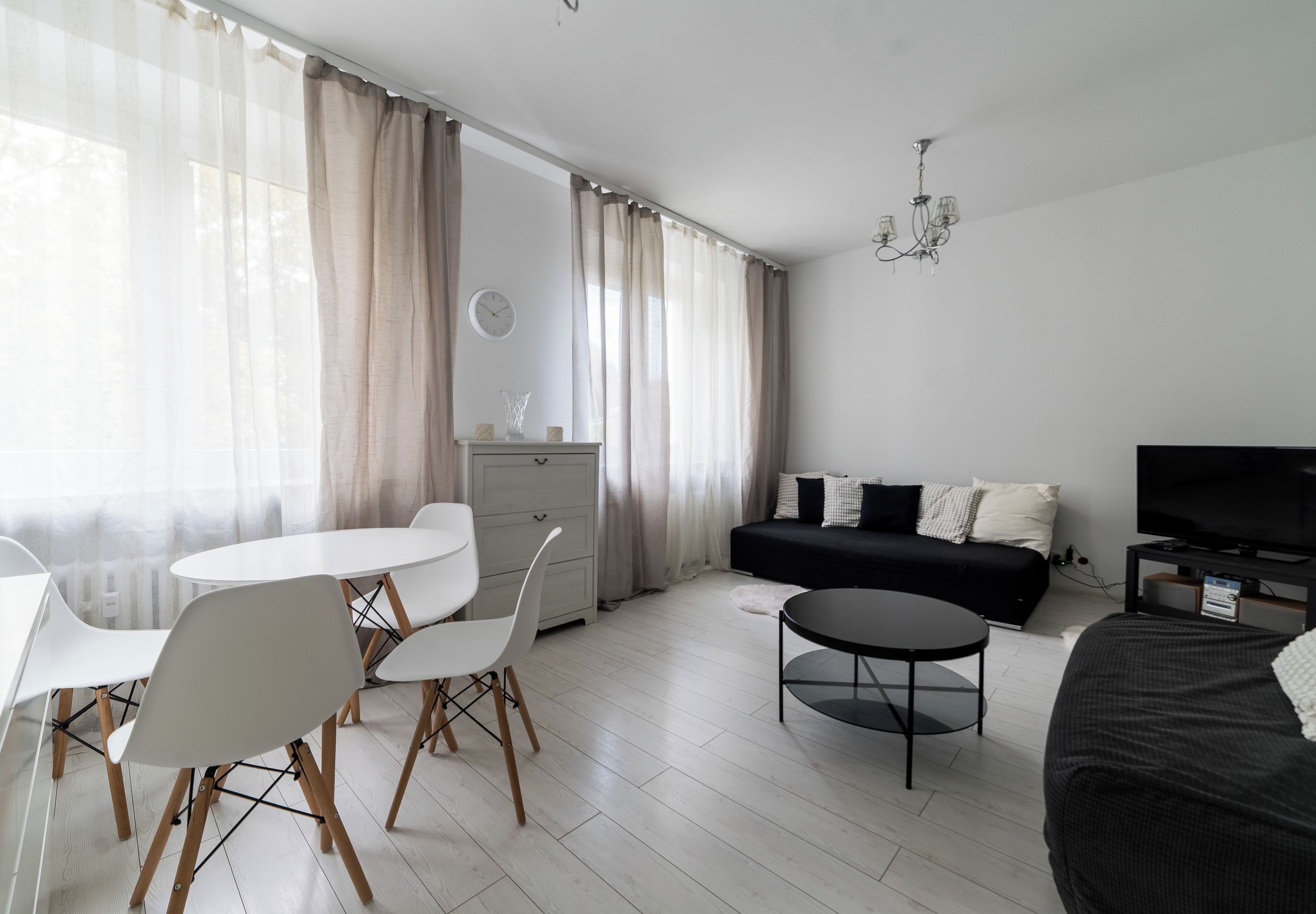 A modern living room with a dining area, a sofa, a TV, and a chandelier.