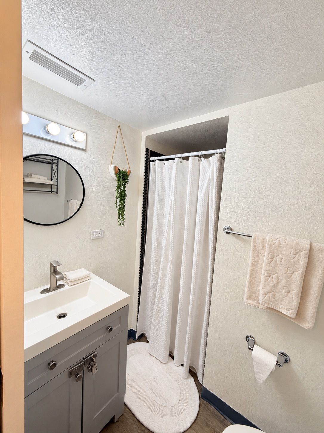Un baño con lavamanos blanco, espejo y toallero.