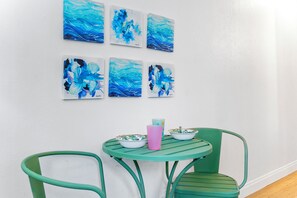 Um quarto com parede branca, uma mesa redonda com duas cadeiras e seis quadros de cenas aquáticas azuis.