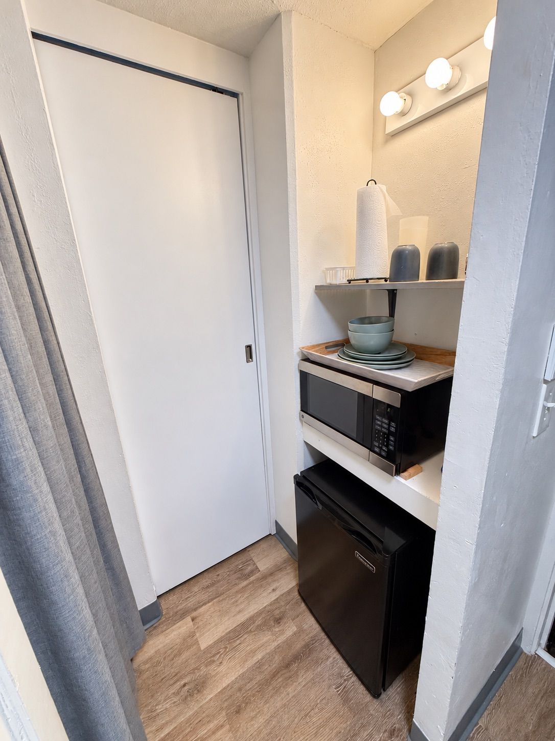 A compact kitchen with a microwave, dishwasher, and a shelf with kitchenware.