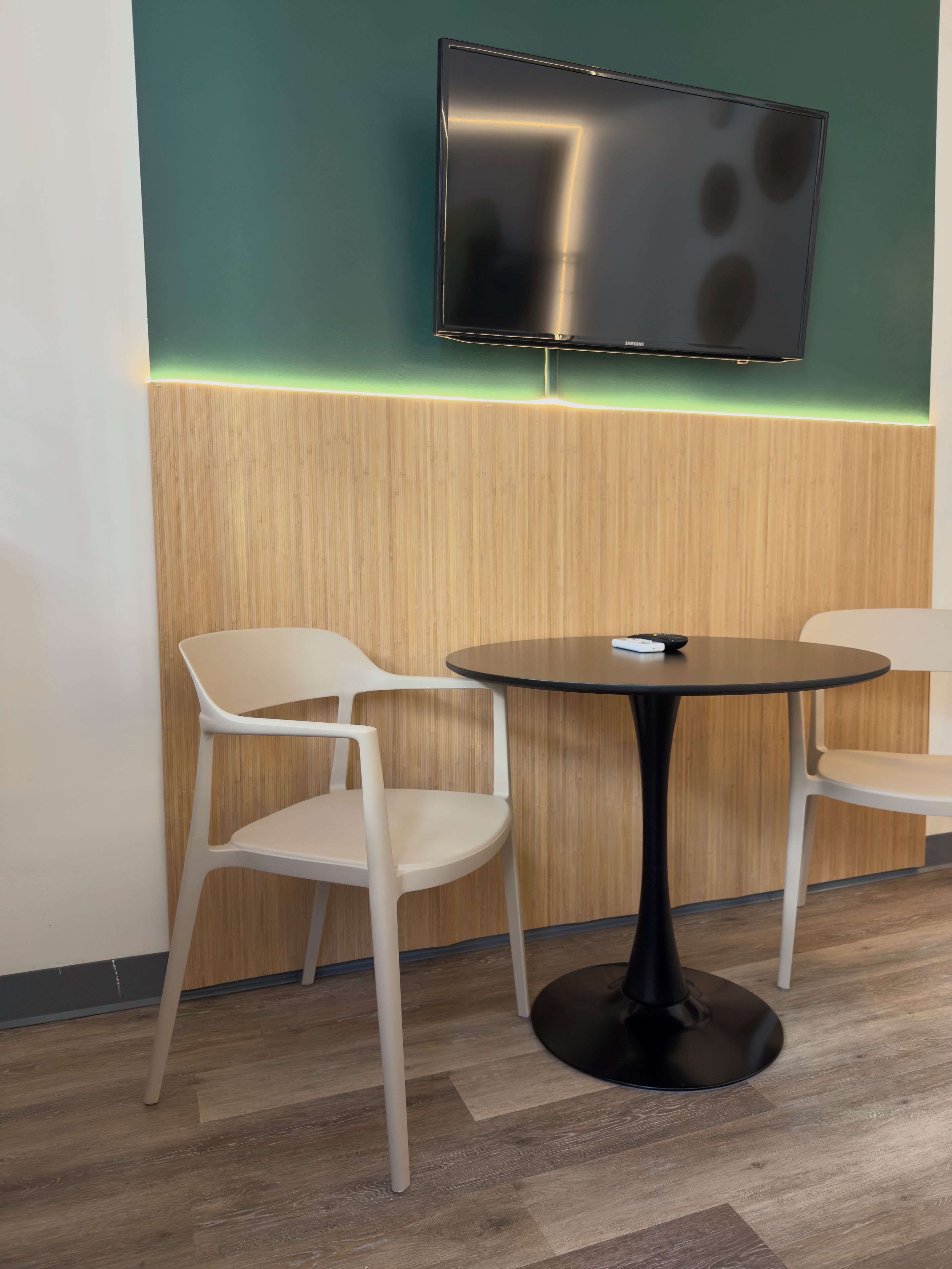 Una habitación moderna con una mesa redonda, dos sillas, un televisor de pantalla plana montado en la pared y una pared de acento de madera con una tira de luz de neón.