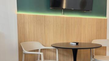 Una habitación moderna con una mesa redonda, dos sillas, un televisor de pantalla plana montado en la pared y una pared de acento de madera con una tira de luz de neón.
