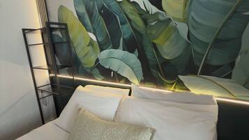 A hotel room with a large bed, white bedding, a headboard with a leaf pattern, and a black metal shelf unit.