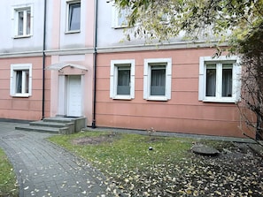 Ein Gebäude mit einer rosafarbenen Fassade, weiß umrandeten Fenstern und einer Tür mit einer kleinen Veranda.