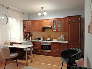 Cocina compacta con armarios de madera, estufa a gas, microondas y un comedor con mesa y sillas.