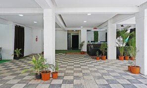 Uma área de recepção com piso xadrez, plantas em vasos, um balcão de atendimento e um extintor de incêndio.