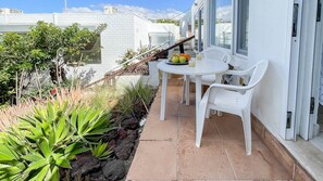 A patio with a table and chairs, a small garden with plants, and a white building in the background. - Nueva Suecia 716 Studio (San Agustin)