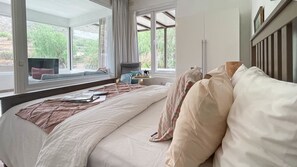 Une chambre avec un grand lit, une fenêtre donnant sur un paysage verdoyant, une table de chevet avec une lampe et une armoire.