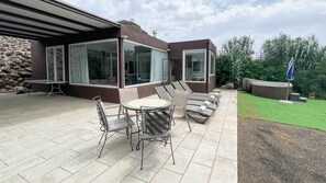 Une terrasse avec une table et des chaises, un mur en pierre et une pelouse avec un jacuzzi.