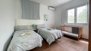 A room with two beds, a crib, a window, and a wall-mounted air conditioner. - Villa Barranco de los Cernícalos - 2-Bedroom Cabin (Vegas, Las (Valsequillo))