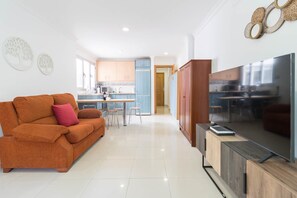 A modern living room with a sofa, a flat-screen TV, and a dining area with a kitchen in the background. - Sagasta Canteras Apartment (Palmas De Gran Canaria, Las)