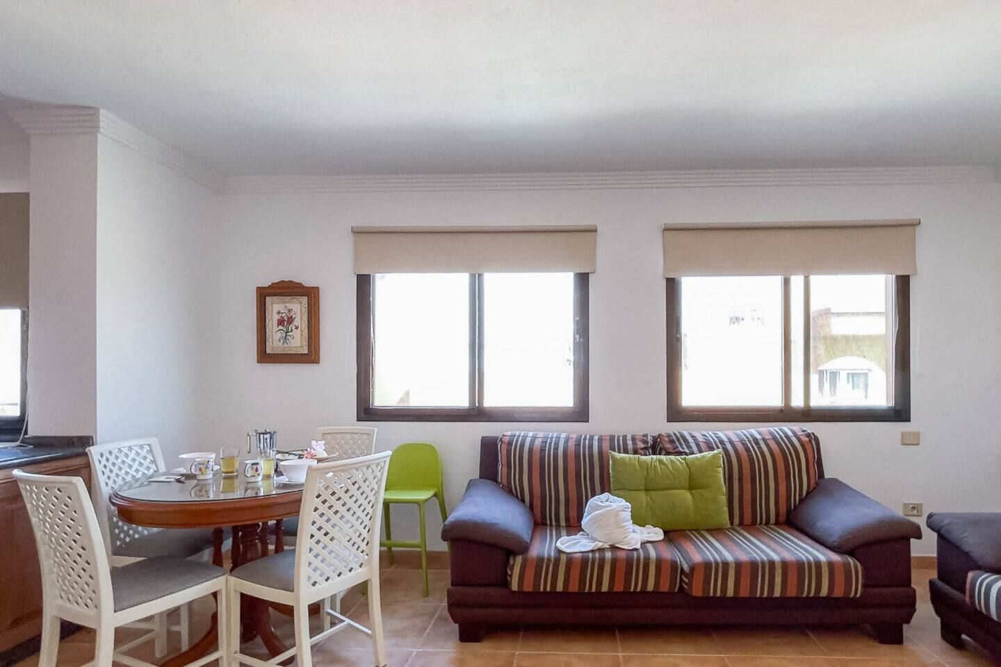 Ein Wohnzimmer mit einer Couch, einem Esstisch mit Stühlen und zwei Fenstern.
