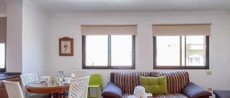 Una sala de estar con un sofá, una mesa de comedor con sillas y dos ventanas.
