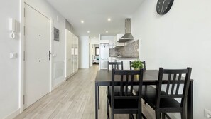 A modern kitchen with a dining area, white cabinetry, and a clock on the wall. - Guanarteme Vista Surf, Las Canteras 2 (Palmas De Gran Canaria, Las)