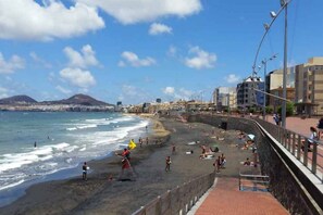 A beach with a stone wall, people, and buildings in the background. - Guanarteme Vista Surf, Las Canteras 2 (Palmas De Gran Canaria, Las)