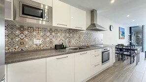Eine moderne Küche mit weißen Schränken, einer Edelstahl-Mikrowelle und einer gemusterten Spritzschutzwand.